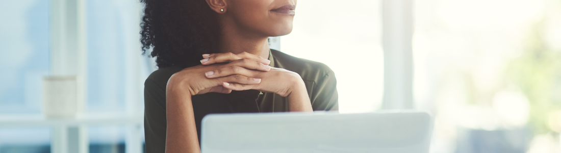 woman sitting in front of laptop with fingers laced together, looking to the side with a small smile